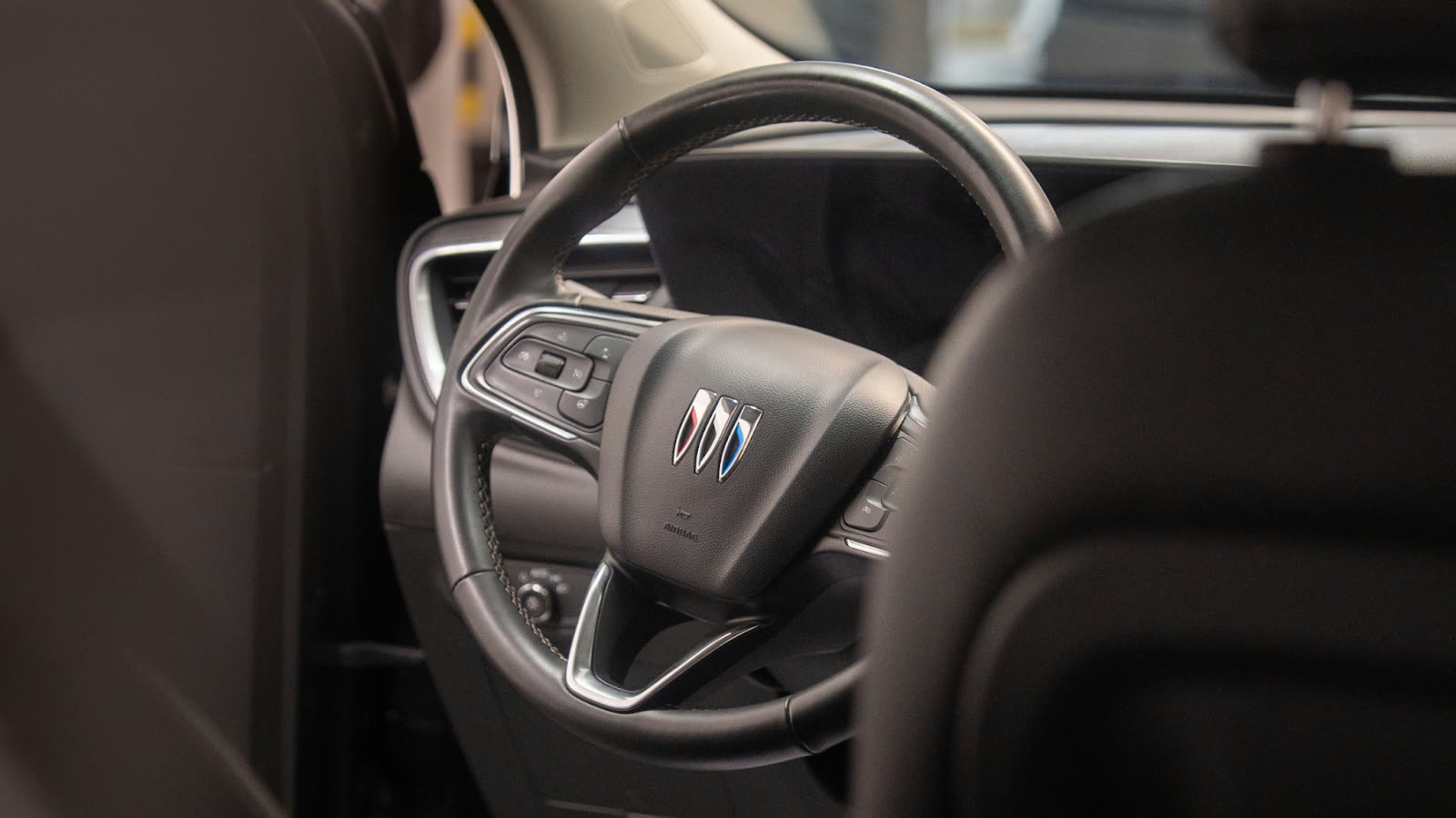 Interior view of a vehicle steering wheel with control buttons and a centered emblem, highlighting a clean dashboard and modern design.