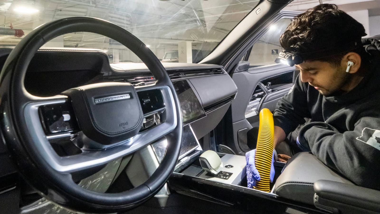 ALPHASHINE detailer cleaning rear floor area of a car interior with a vacuum and inspection light, targeting debris in carpeted surfaces.