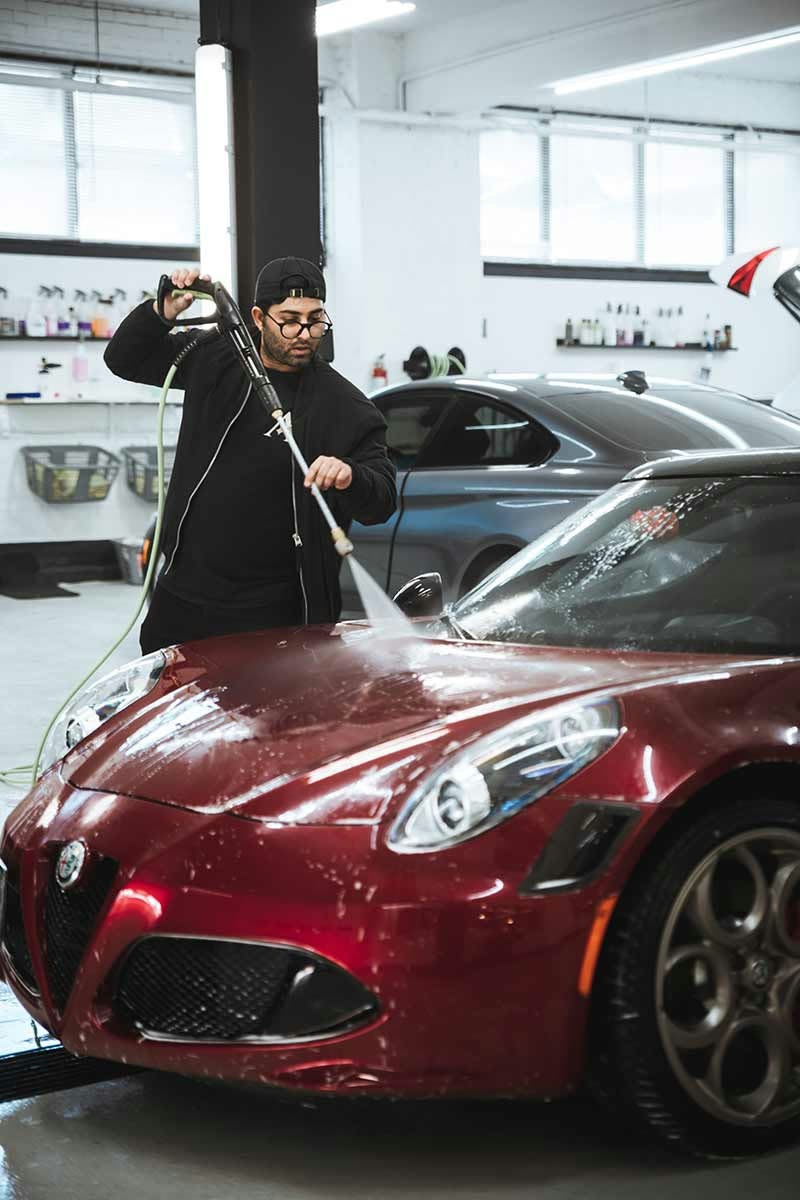 Detailing professional pressure washing a red Alfa Romeo inside a car detailing Toronto studio. The scene showcases best car detailing Toronto standards and expert Toronto auto detailing methods to restore a spotless finish.