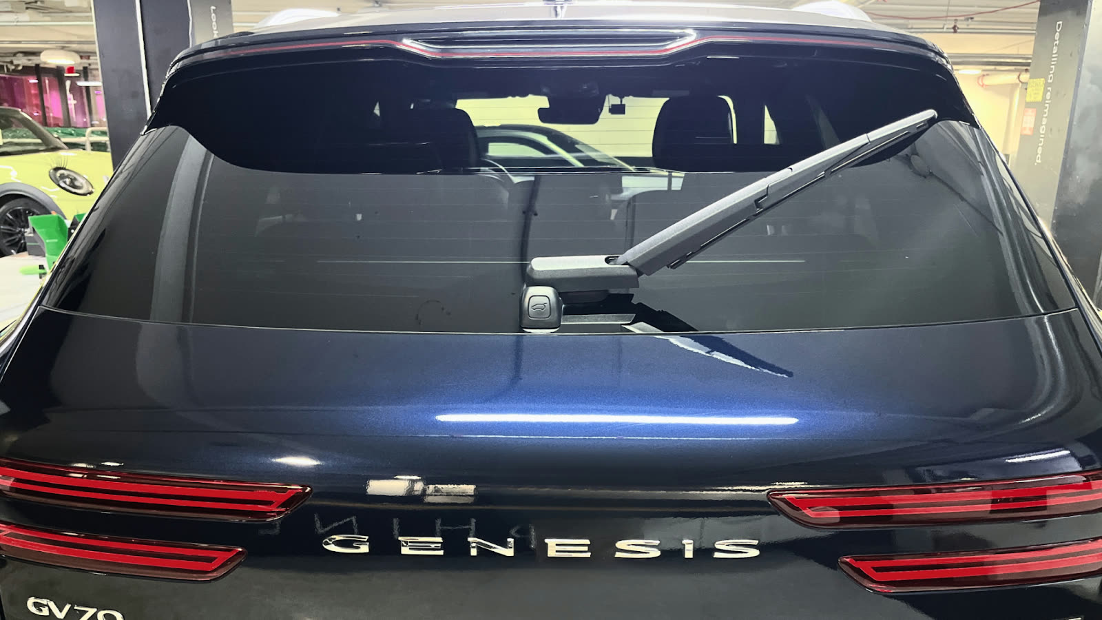 The rear of a dark blue Genesis GV70 SUV after professional detailing, showcasing a spotless, glossy finish under indoor lighting at ALPHASHINE’s Toronto location.