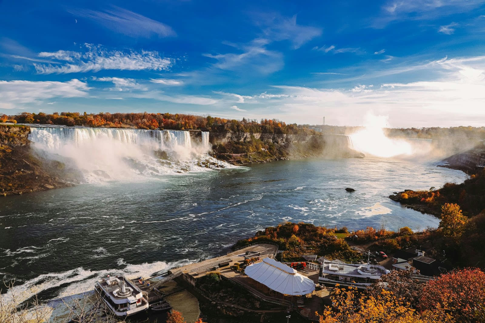 Stunning view of Niagara Falls near Toronto, with mist rising and vibrant fall colors under a bright blue sky.